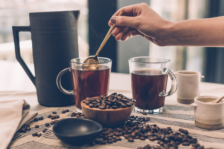 A woman stirring a cup of coffee with other drinkware on the table