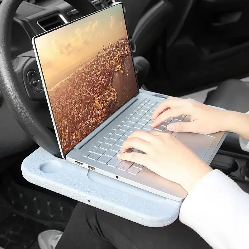 a person typing on a laptop resting on the Car Steering Wheel Tray